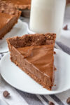 A slice of vegan chocolate pie on a white plate with a glass of milk