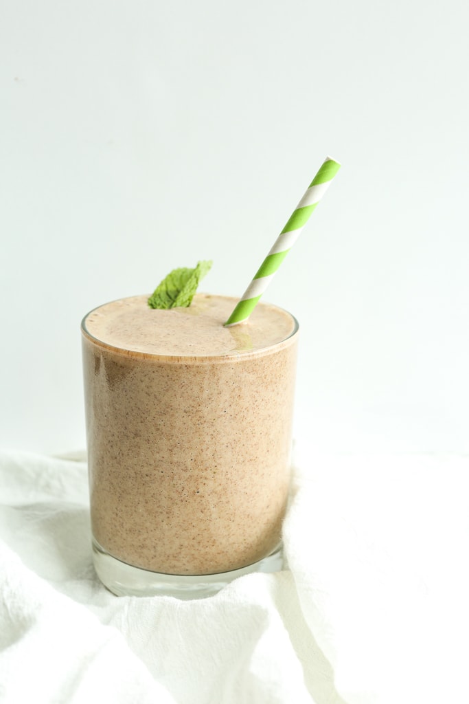 a smoothie in a glass with a green and white striped straw and a mint leaf