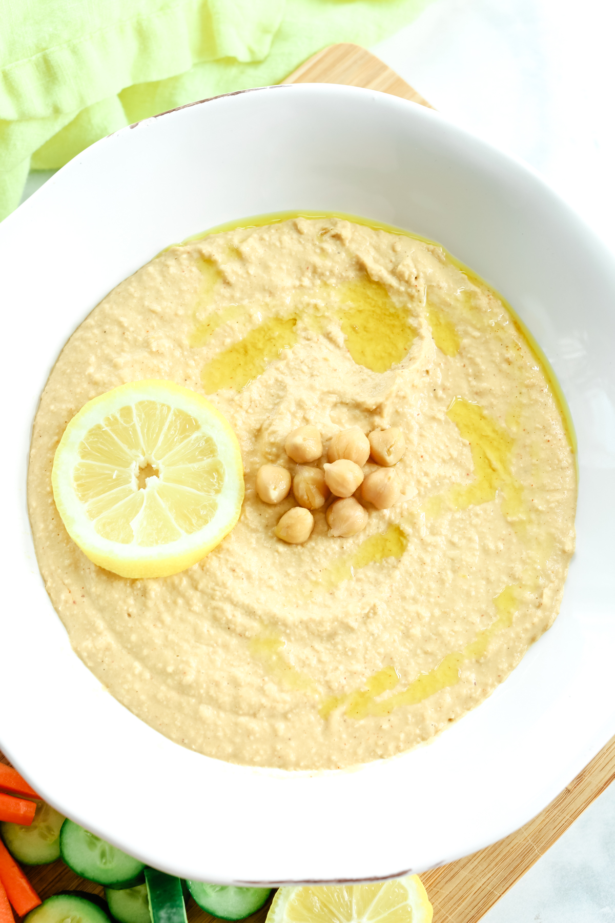 close up photo of lemon hummus with chickpeas and a lemon slice on top with a drizzle of olive oil 