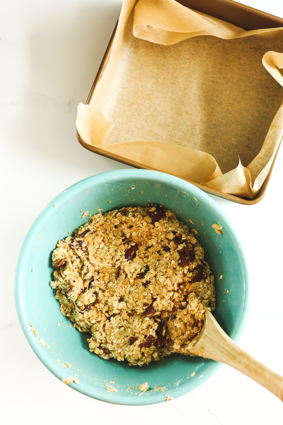 ingredients mixed together in a blue bowl next to a parchment paper lined square pan