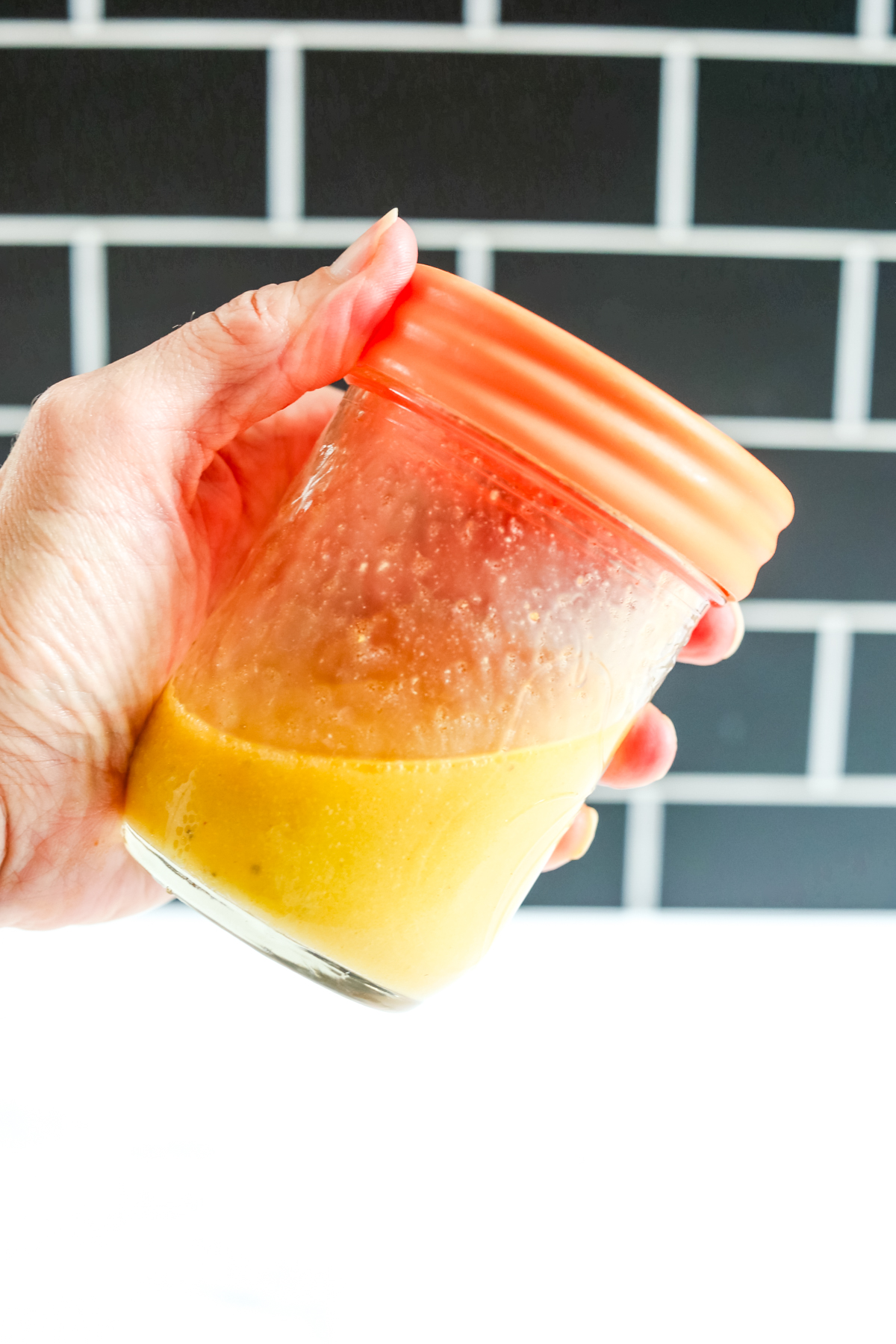 yellow hued salad dressing in a mason jar with a hand holding it