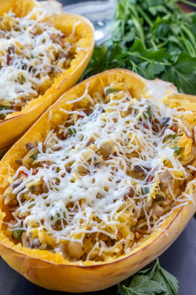 baked spaghetti squash on the table with green leafy parsley and melted cheese on top