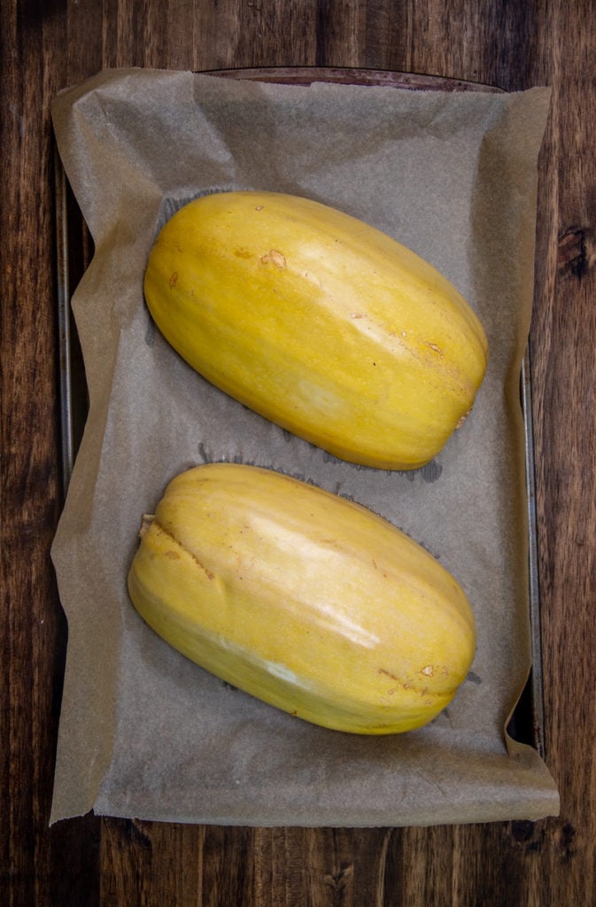 two spaghetti squash halves down on a parchment lined baking sheet