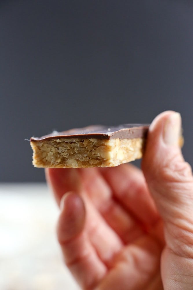 4-ingredient peanut butter granola bar recipe with chocolate, a single bar held in a hand with black background