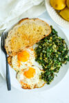 a plate with kale and eggs, a piece of toast, and a black fork