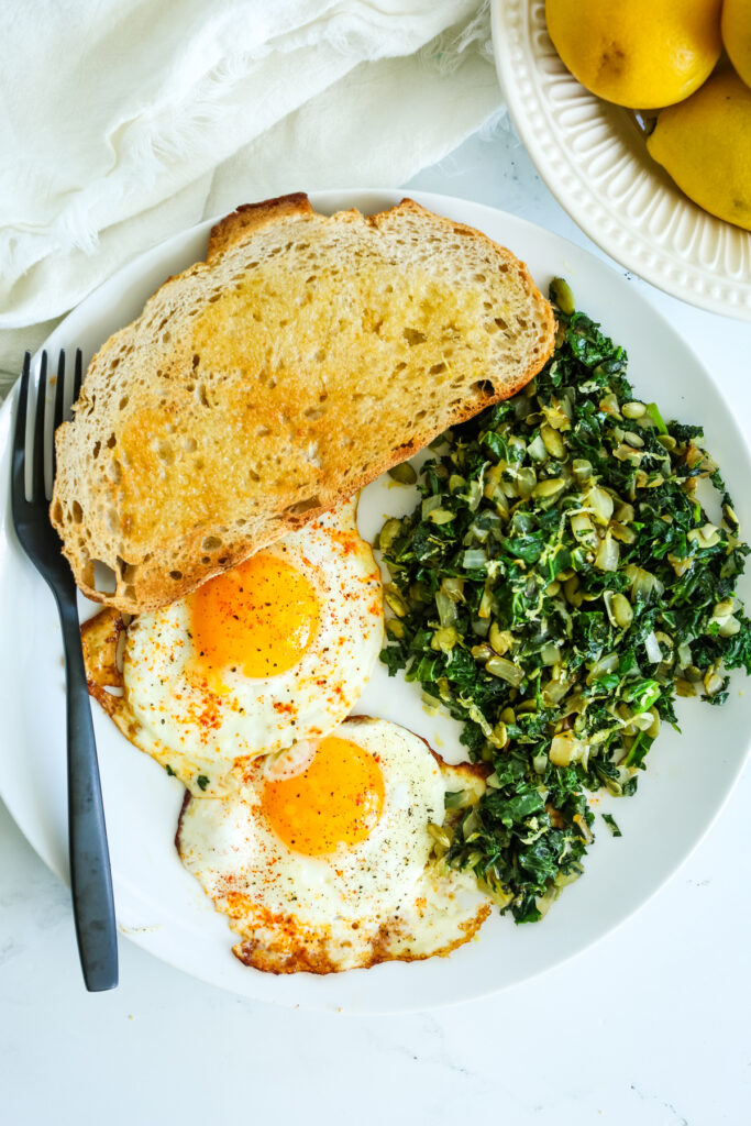 a plate with kale and eggs, a piece of toast, and a black fork