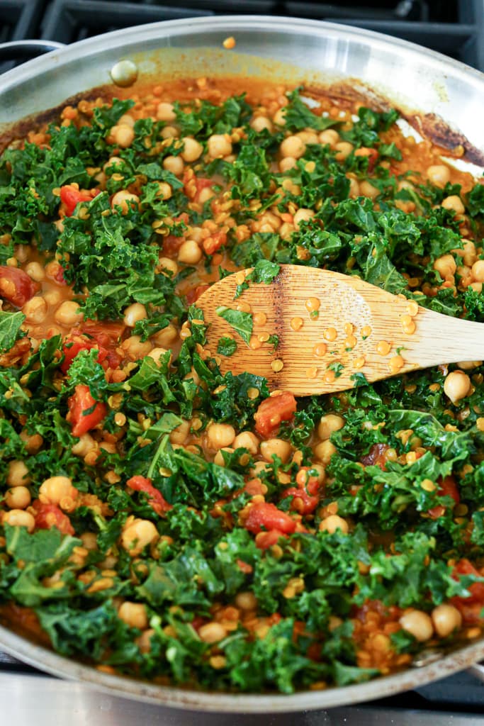 stirring in kale and chickpeas with a wooden spoon