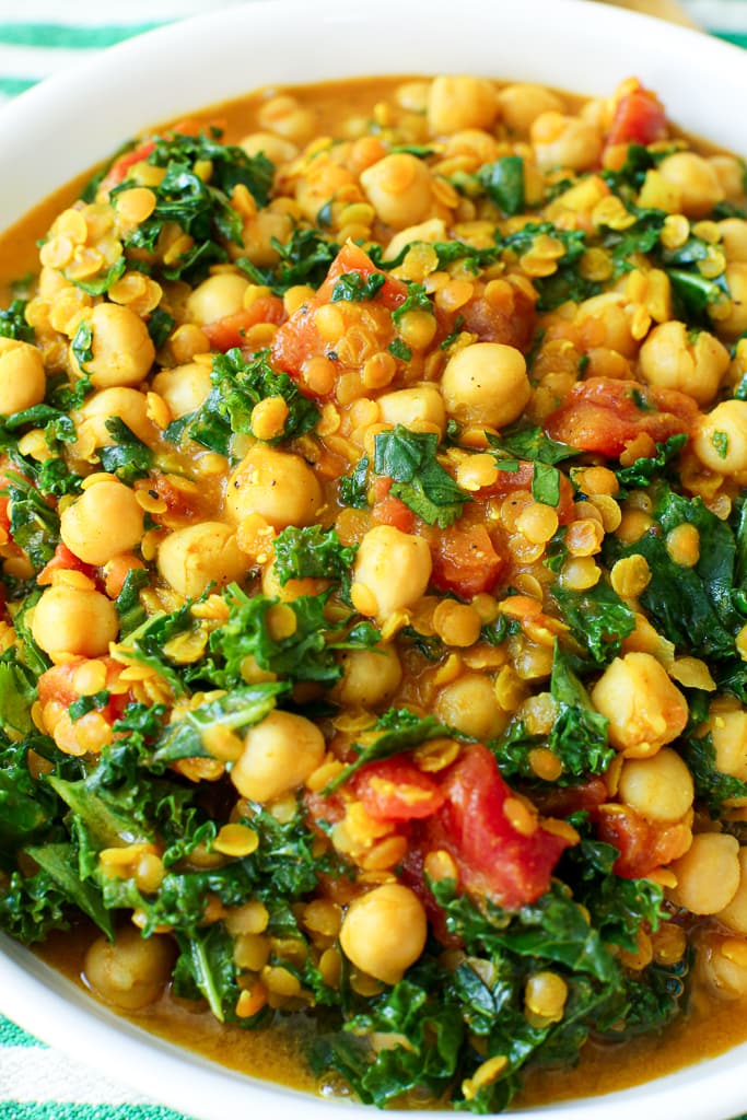 close up shot of chickpeas, kale, and lentils in a white bowl
