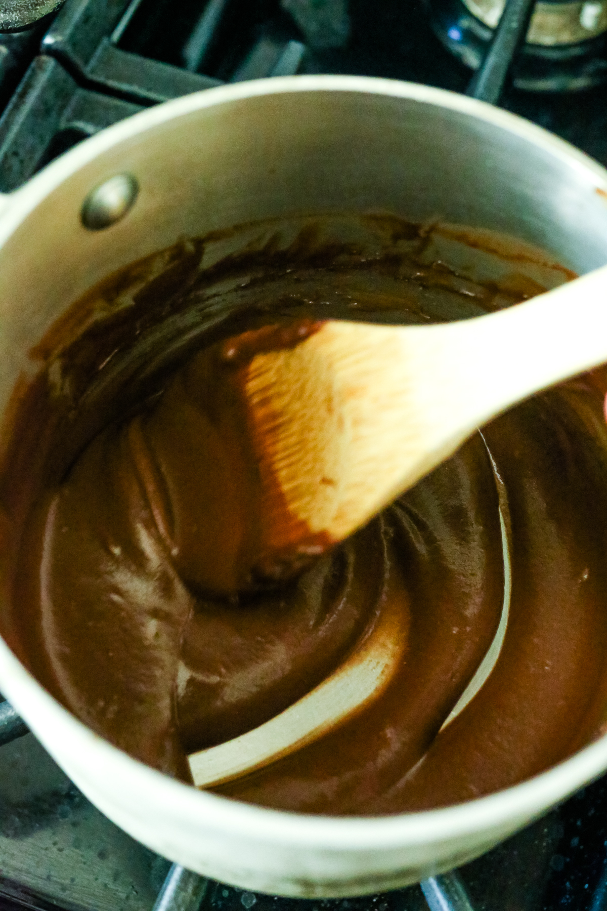 chocolate sauce getting thicker in a saucepan with a wooden spoon