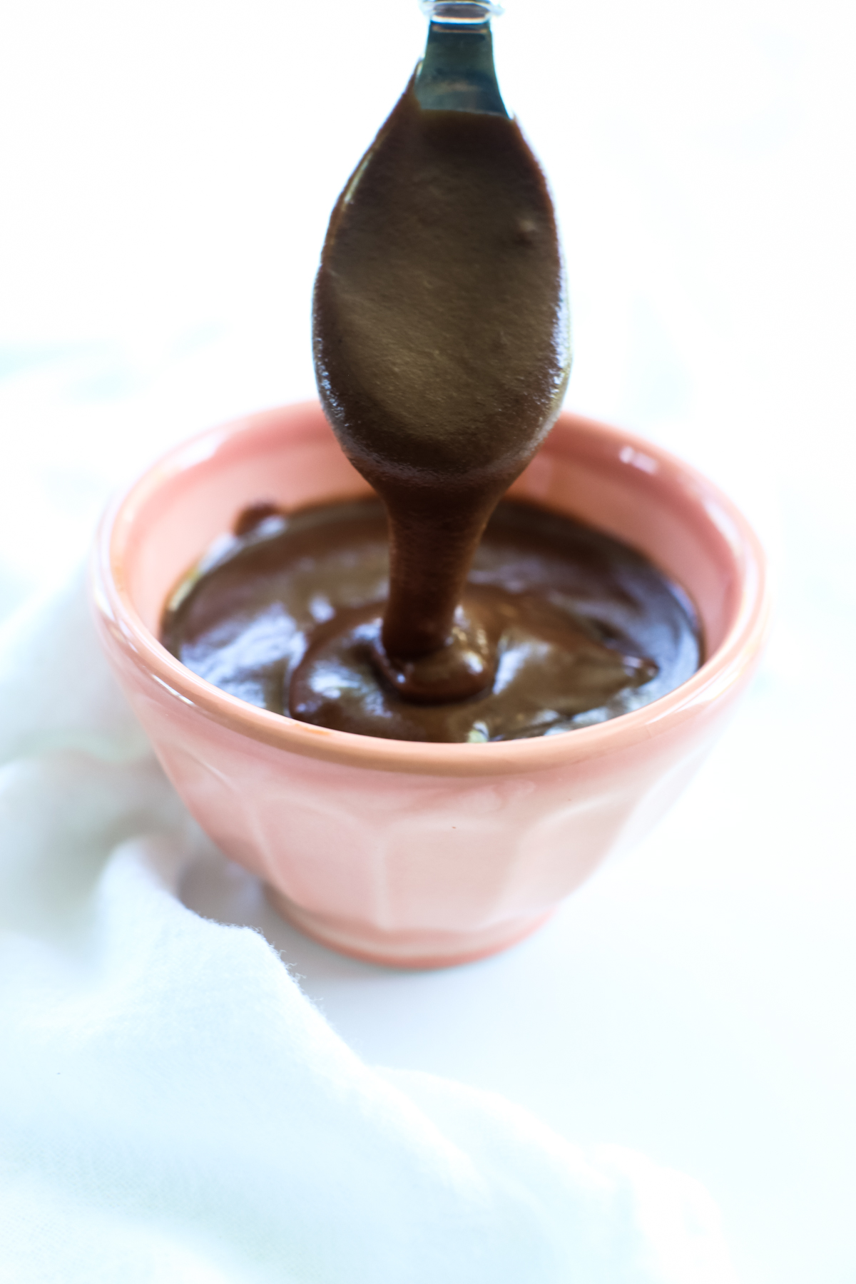 a spoon lifting vegan hot fudge out of a small peach colored bowl