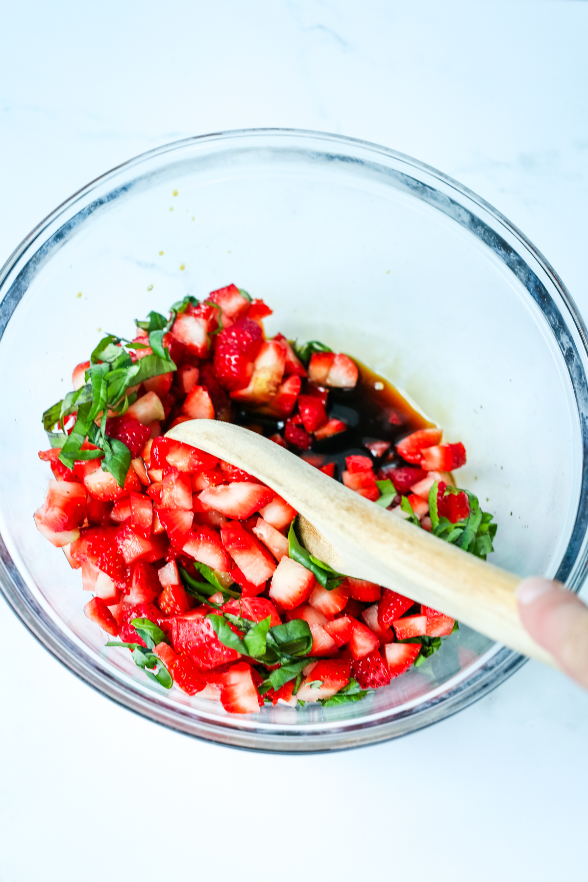 diced strawberries, basil leave strips, and balsamic vinegar in a small glass bowl being mixed with a wooden spoon
