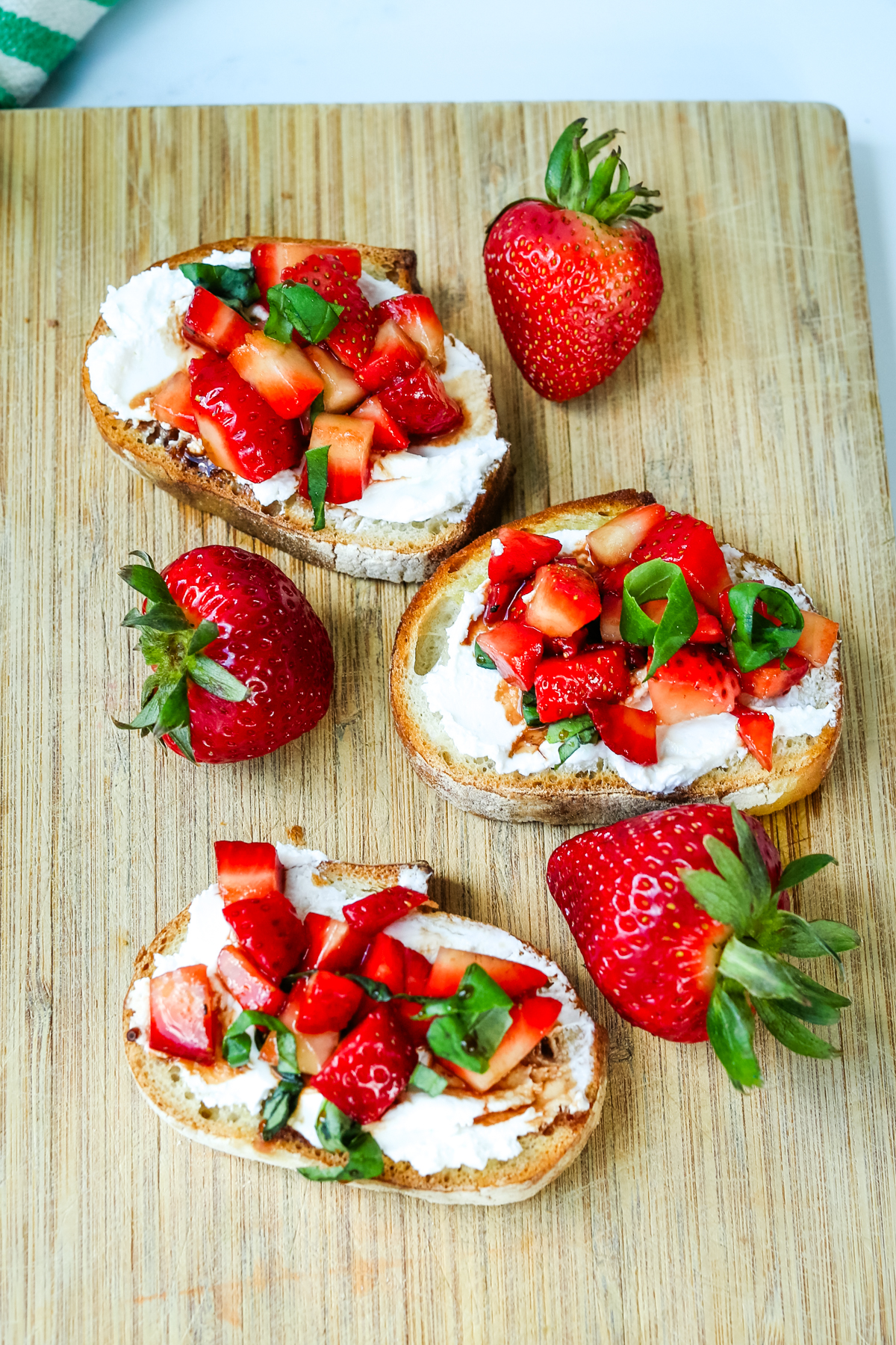 three slices of strawberry bruschetta on a cutting board with whole strawberries in between