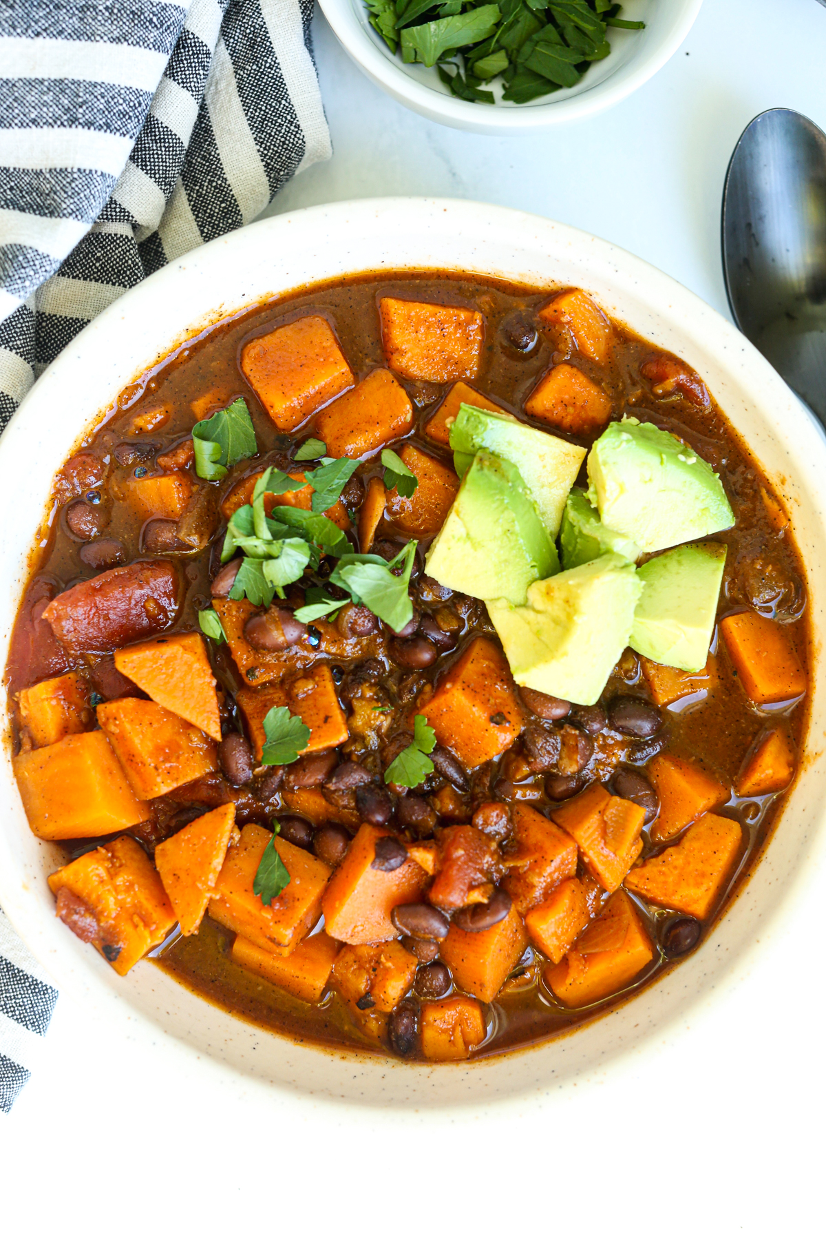 a bowl of sweet potato and black bean chili with cilantro and avocado on top