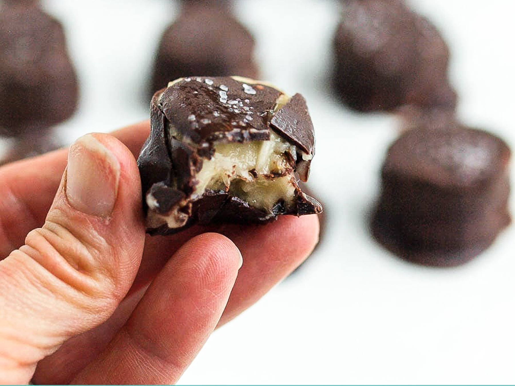 a chocolate covered banana bite in the hand of a person with a bite out of it