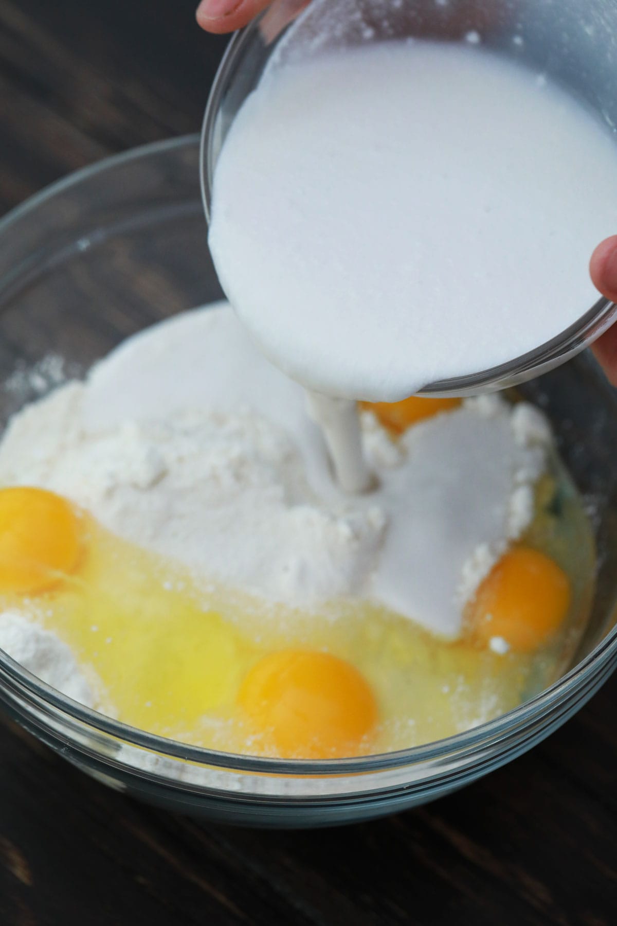 pouring milk into a bowl of flour with eggs