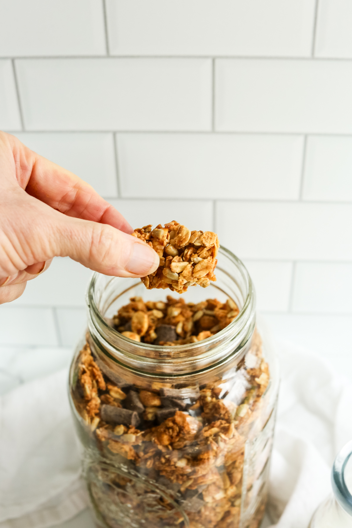 a finger and thumb holding a chunk of granola from a glass mason jar