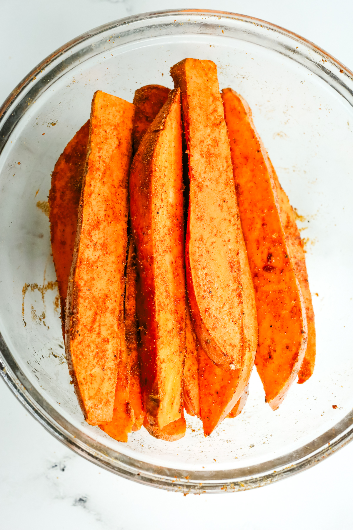 sweet potatoes coated with oil and spices in a glass bowl