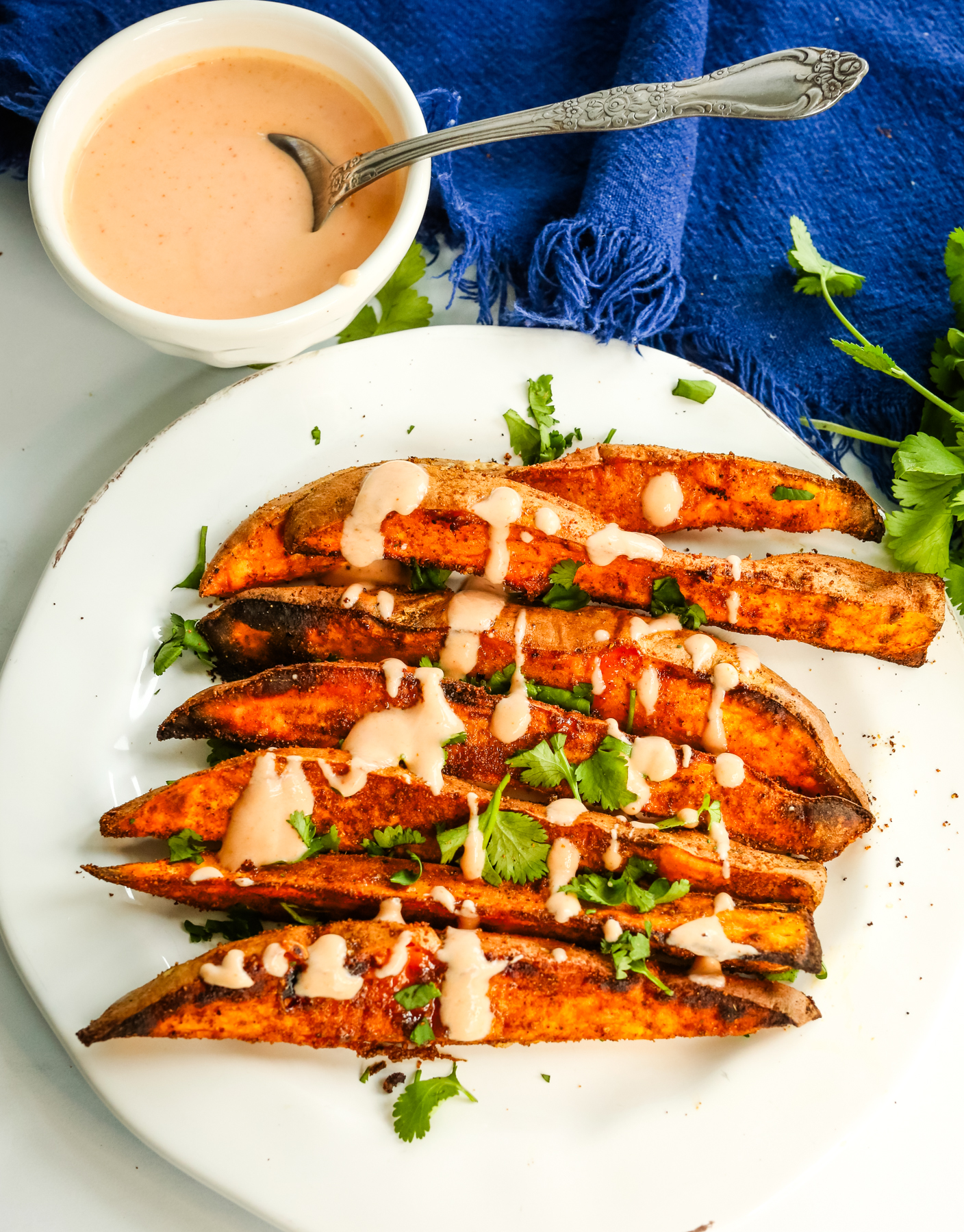 a plate of sweet potato wedges topped with a orange hued sauce and chopped cilantro