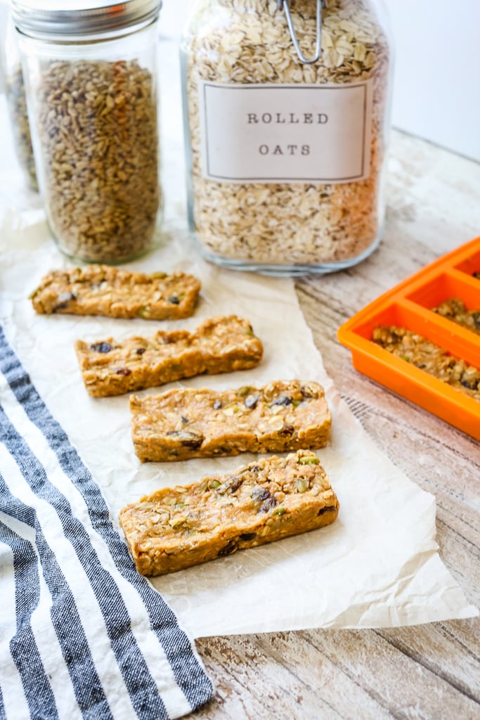 4 granola bars in a staggered line with a glass jar of oats and seeds in the background
