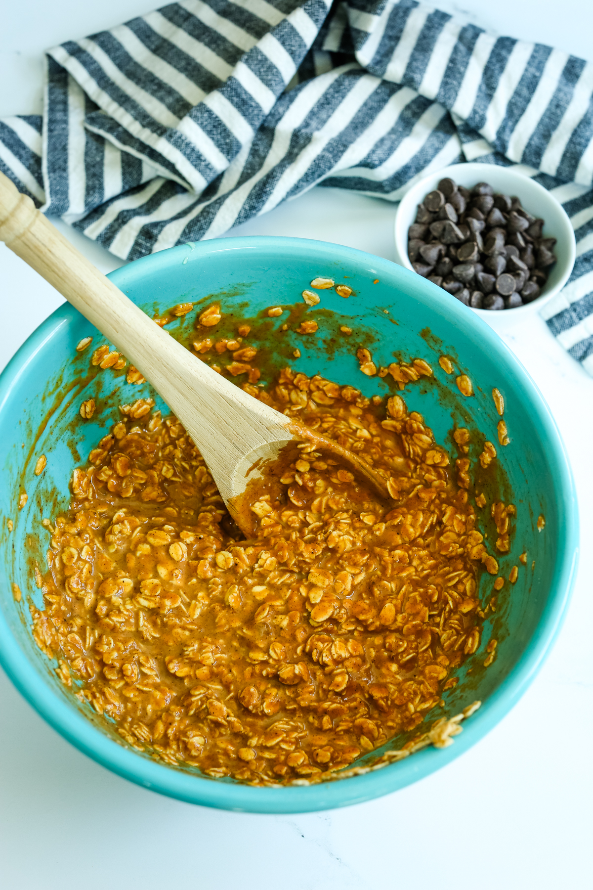 An orange batter with oats in a turquoise bowl with a wooden spoon