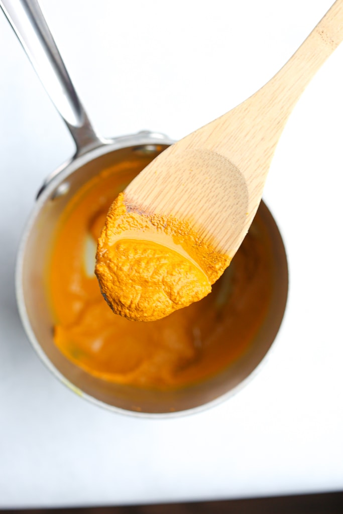 turmeric paste on a spoon above a pan of turmeric paste