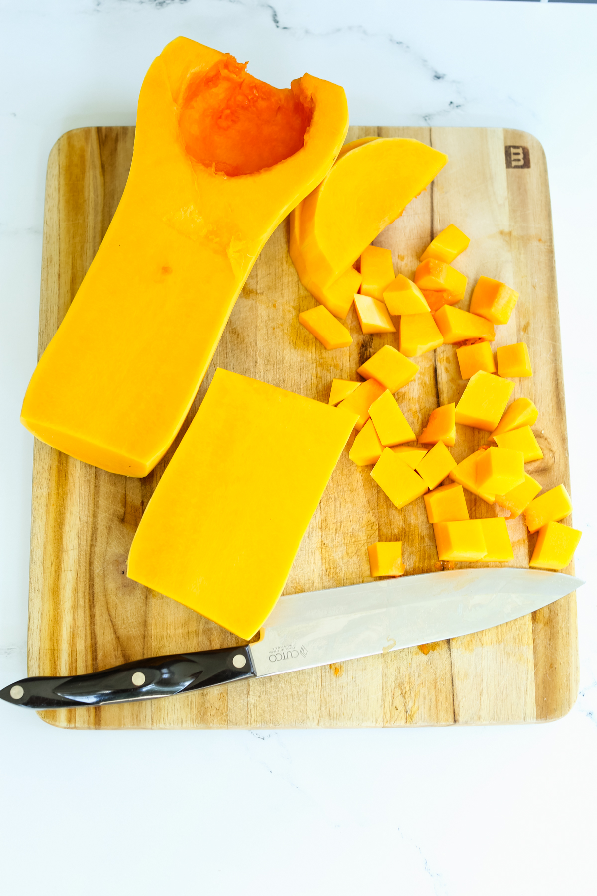 butter squash on a cutting board with seeds removed and partially cut into cubes
