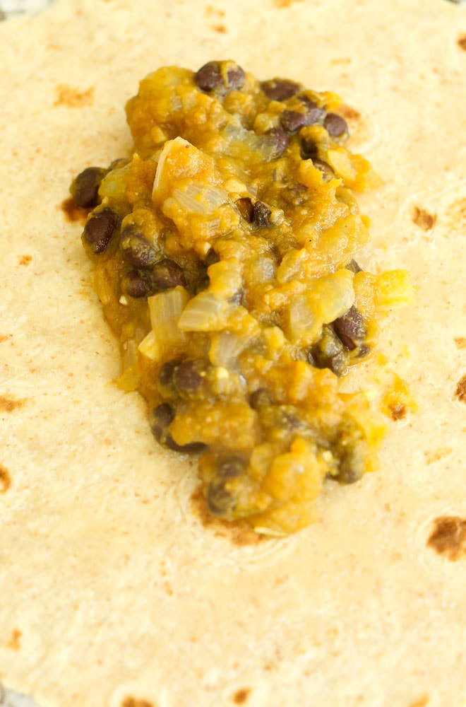 Adding the filling to the tortillas in the Butternut Squash Black Bean Enchilada Recipe