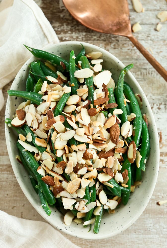 Garlic Butter Green Beans with Toasted Almonds recipe in a bowl with a copper serving spoon