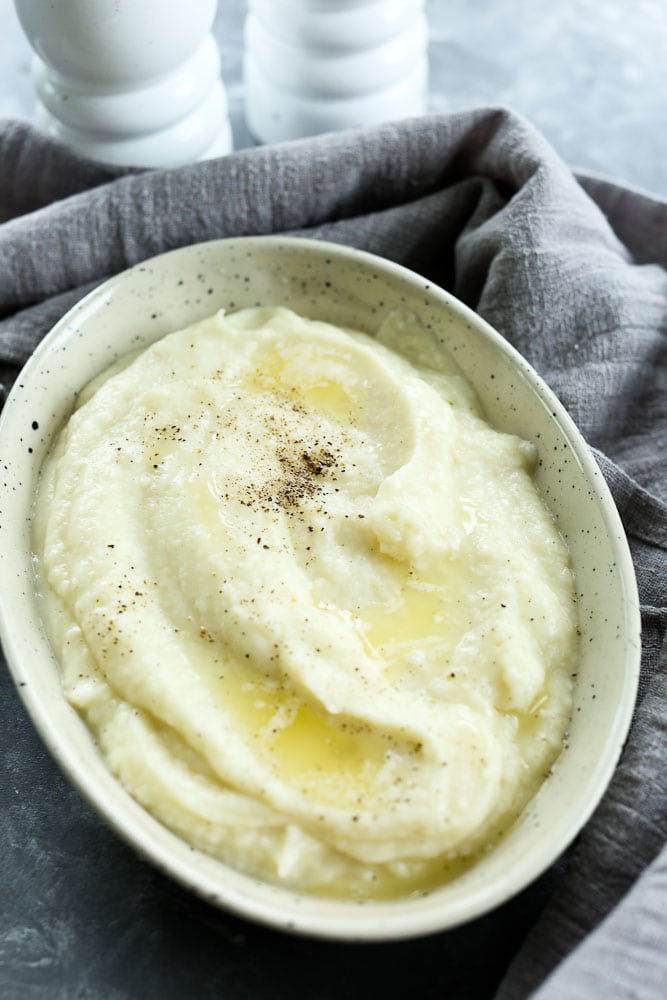 Instant Pot Mashed Cauliflower Recipe--in an oval serving bowl with a grey napkin and a salt and pepper shaker