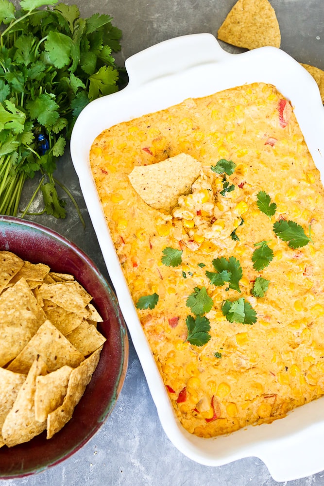 Hot Corn Dip Recipe next to a bowl of chips with a chip in the dip