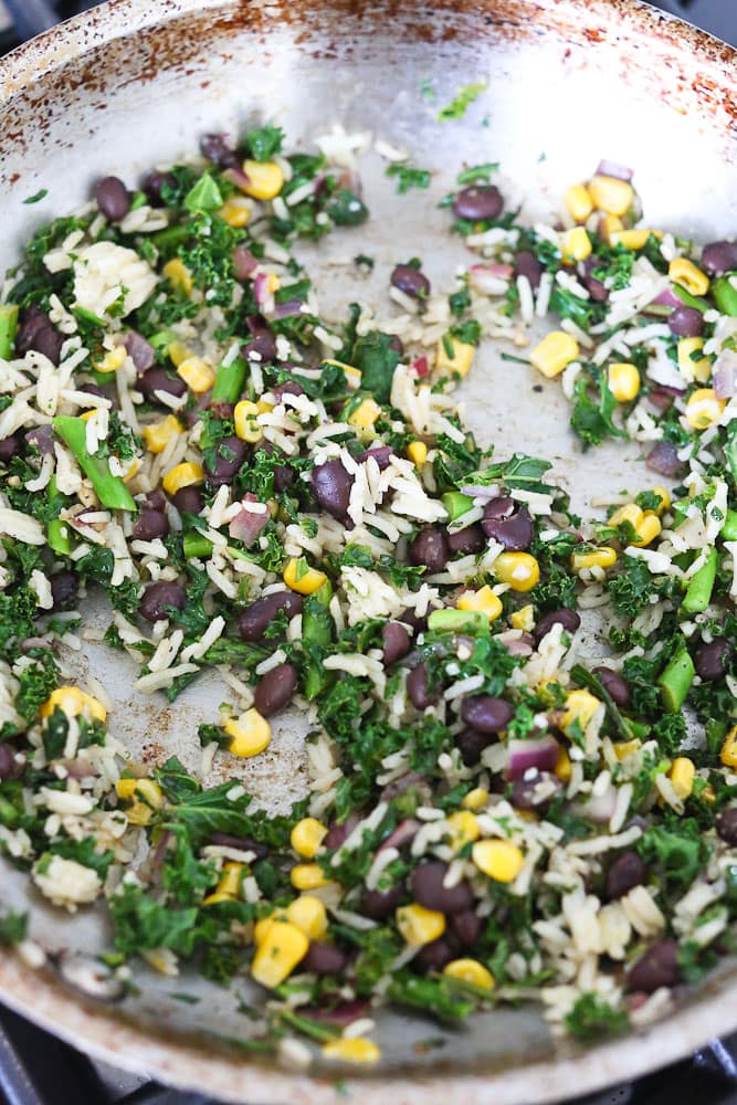 How to make a hummus veggie wrap with kale, spinach, asparagus, rice, beans, and corn getting warm in pan.