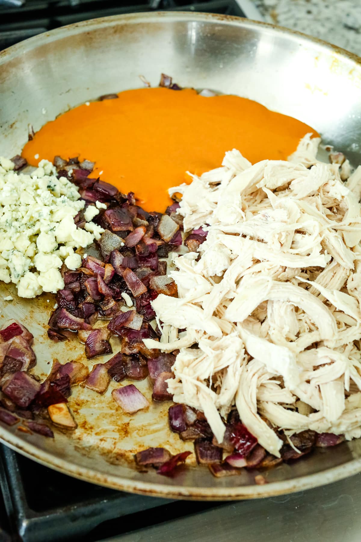 shredded chicken, buffalo sauce, blue cheese, and red onion in a pan