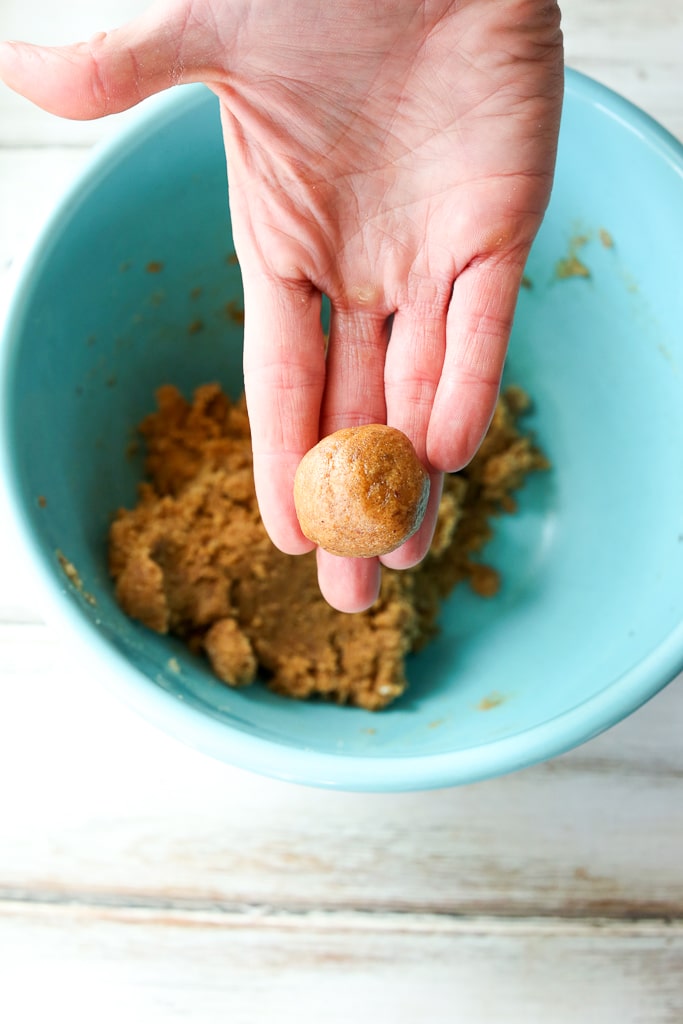 a hand holding a ball of dough with a turquoise bowl filled with dough under it. 