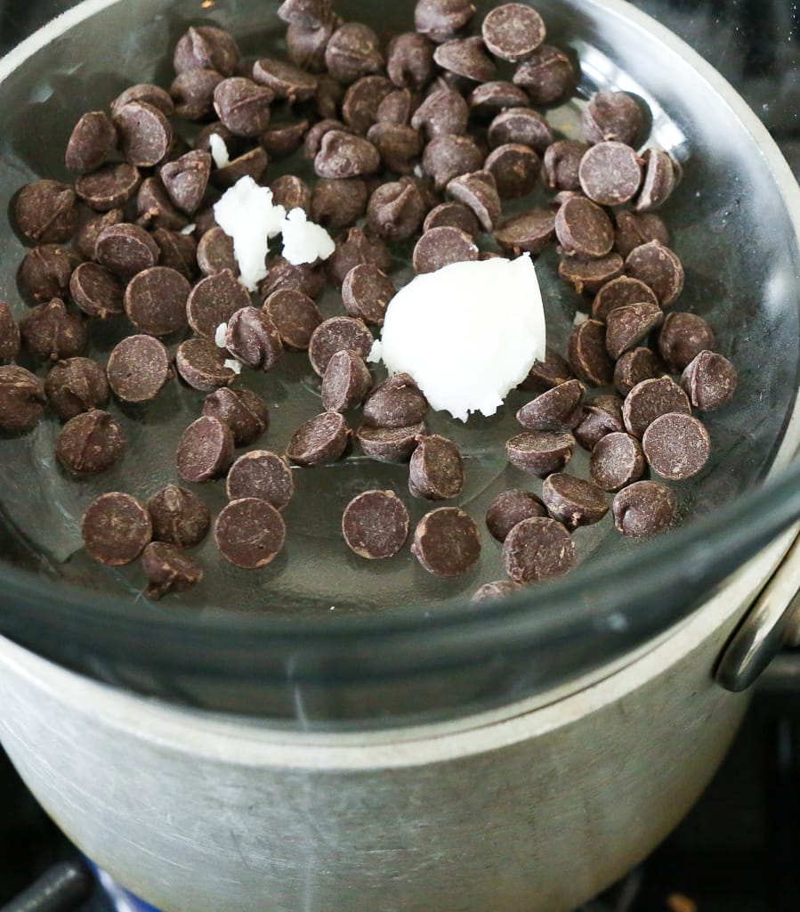 a pan with a glass bowl over it and chocolate chips and coconut oil in the glass bowl 