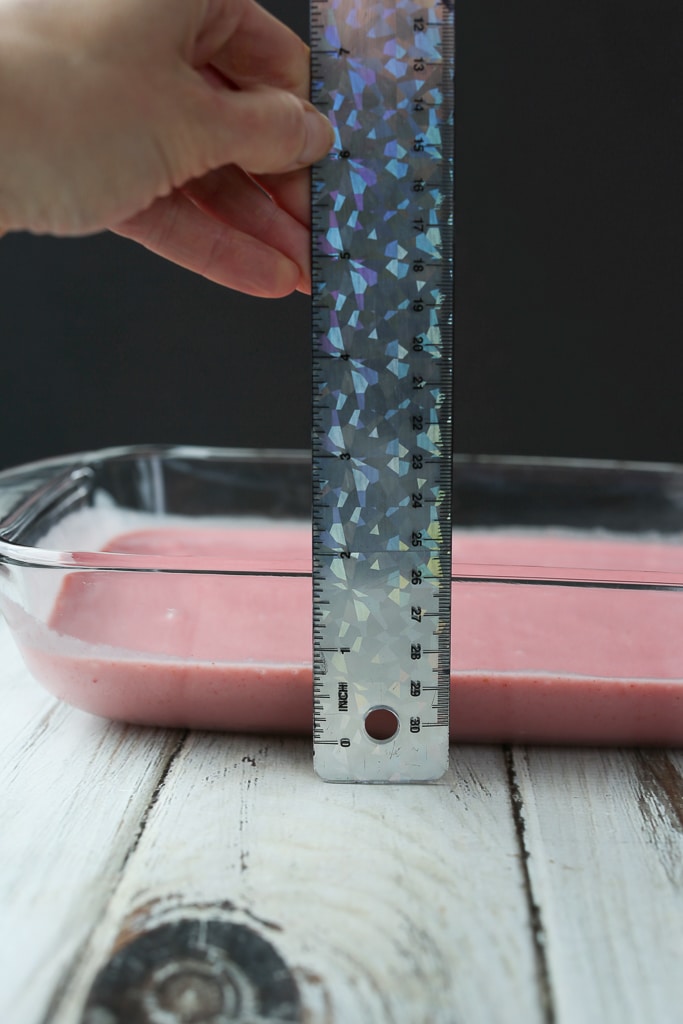 strawberry liquid in a glass pan with a hand holding a ruler showing 1 inch thick
