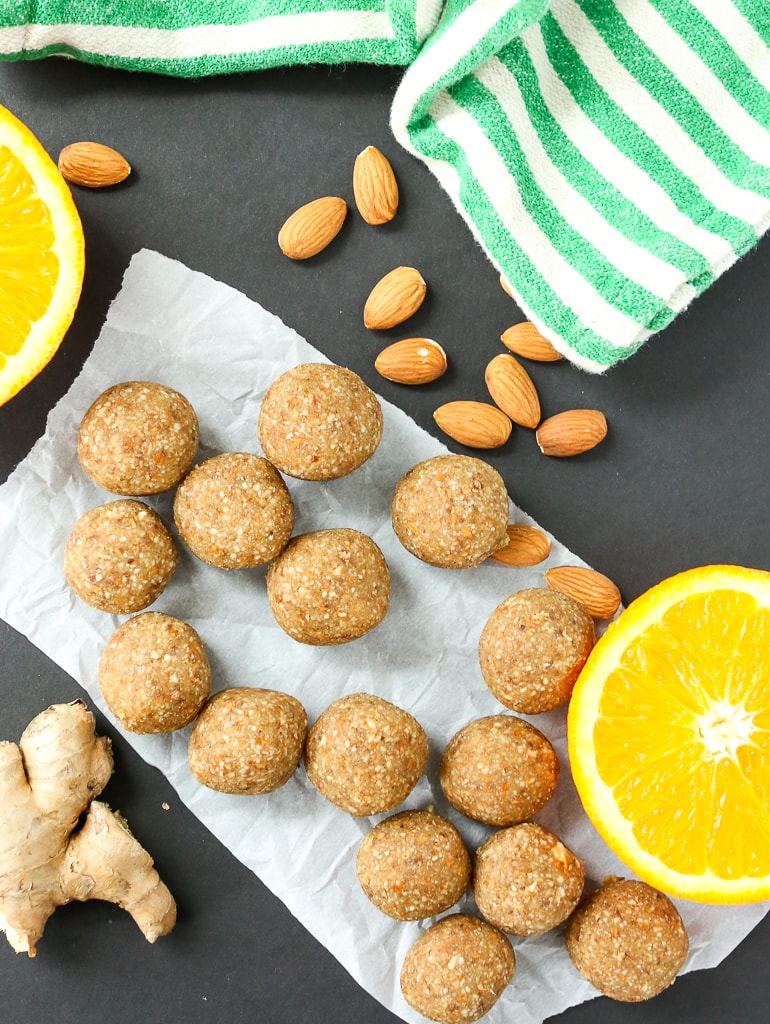 Anti-inflammatory Ginger Energy Balls overhead shot with a cut orange, almonds, fresh ginger, and a green and white striped napkin