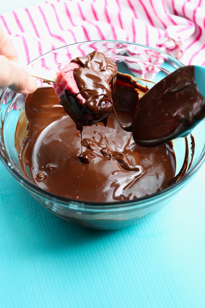 a bowl of melted chocolate with an ice cream bar being dipped