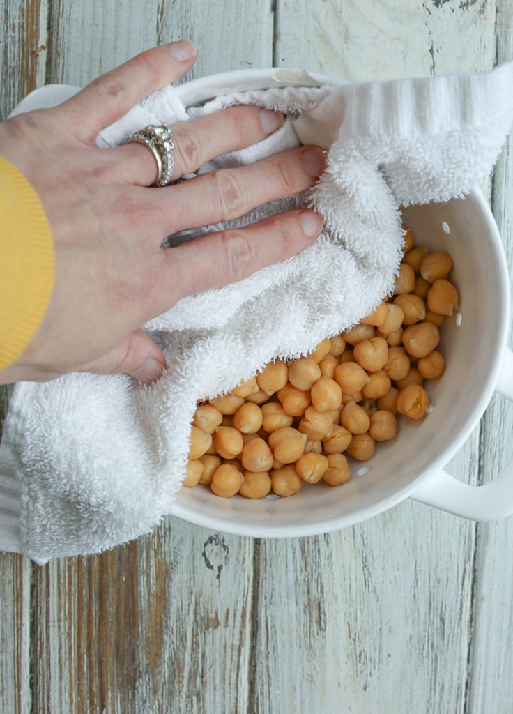 chickpeas in a white colander with a hand drying them with a white towel