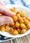 a finger and thumb holding a crispy chickpea with. bowl in the background