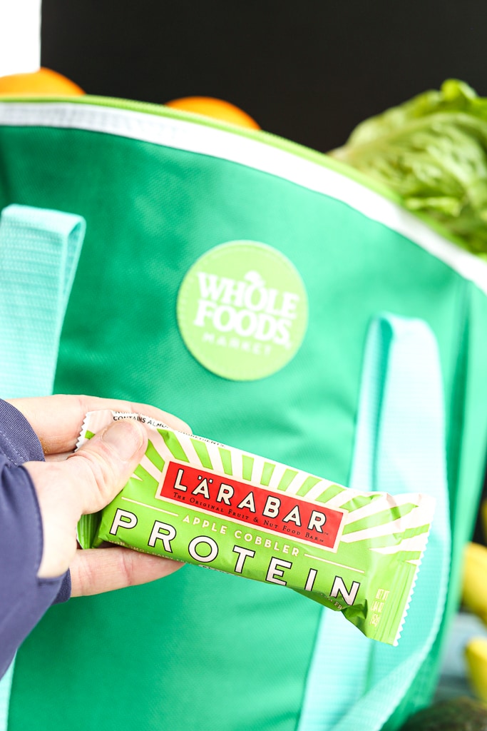 A Larabar protein bar in front of a bag of groceries from Whole Foods