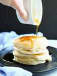 Vegan Pancakes Recipe pouring syrup on the stack of pancakes on a black plate
