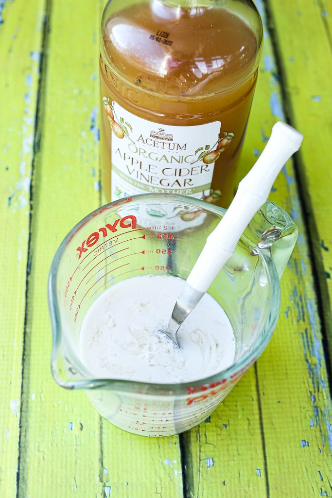 Milk in a glass measuring cup with a spoon and a bottle of apple cider vinegar
