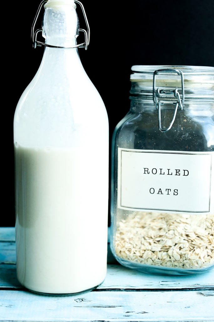 A bottle of oat milk with a jar of rolled oats in the background