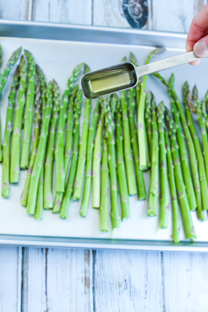 drizzling oil on a pan of raw asparagus 