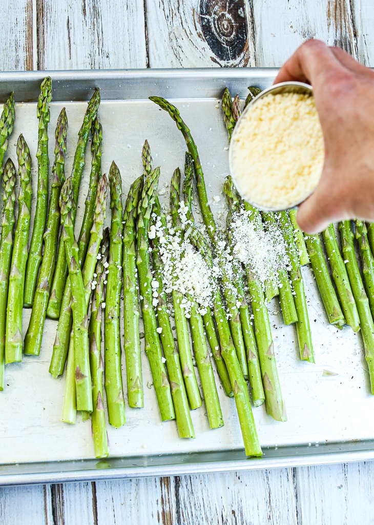 a cup of parmesan cheese being dumped on asparagus