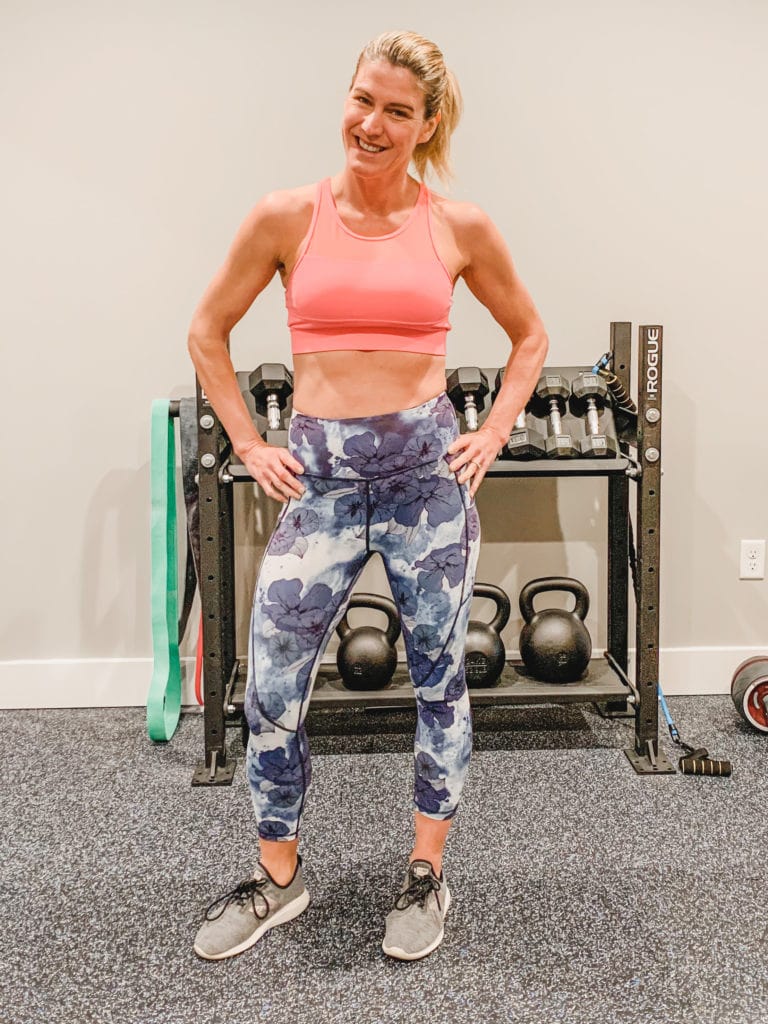 A woman standing with her hands-on her hips wearing floral leggings and a pink sports bra