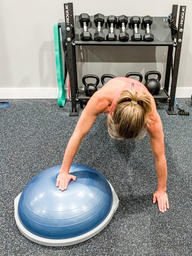 A woman completing a push up with one hand on a Bosu Ball