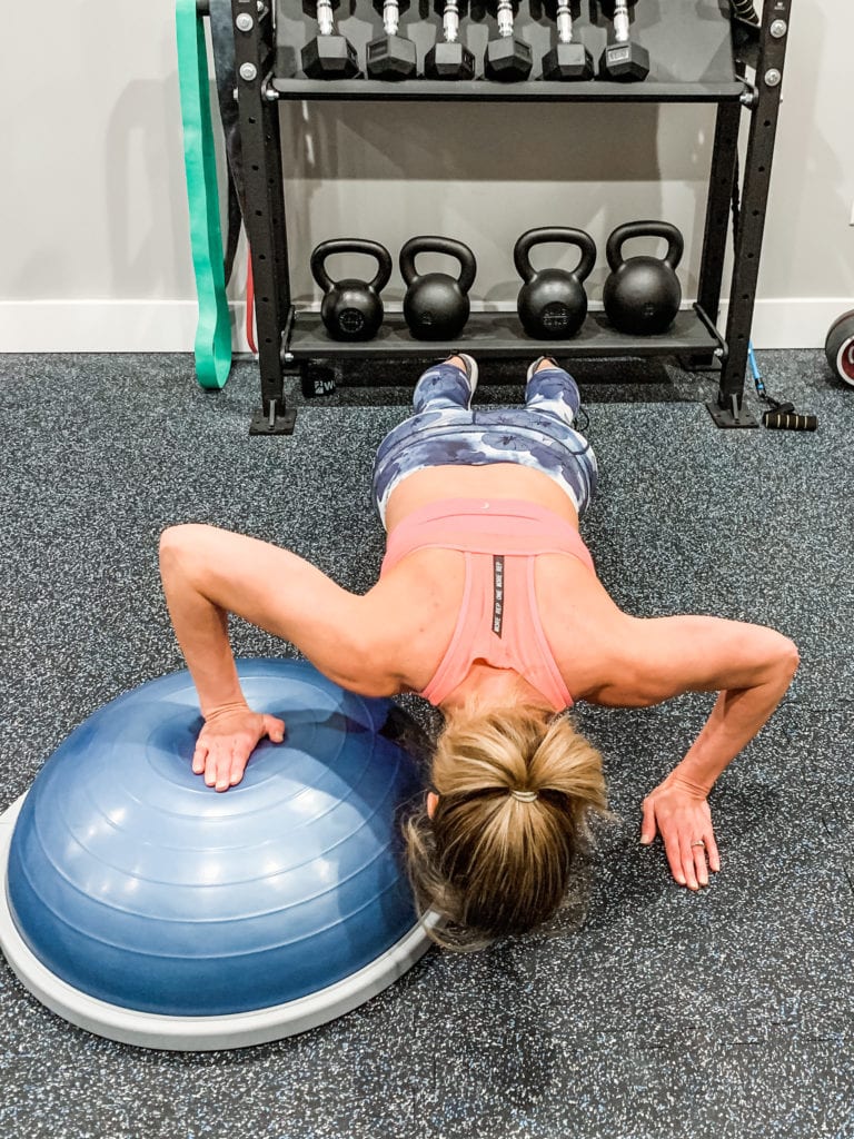 A woman completing a push up with one hand on a Bosu Ball