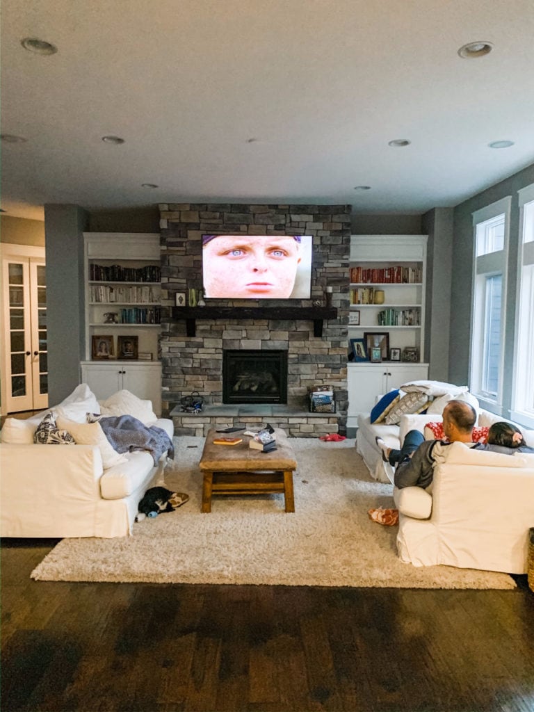 a family in the living room watching a movie on a large screen above fireplace showing Sandlot movie 