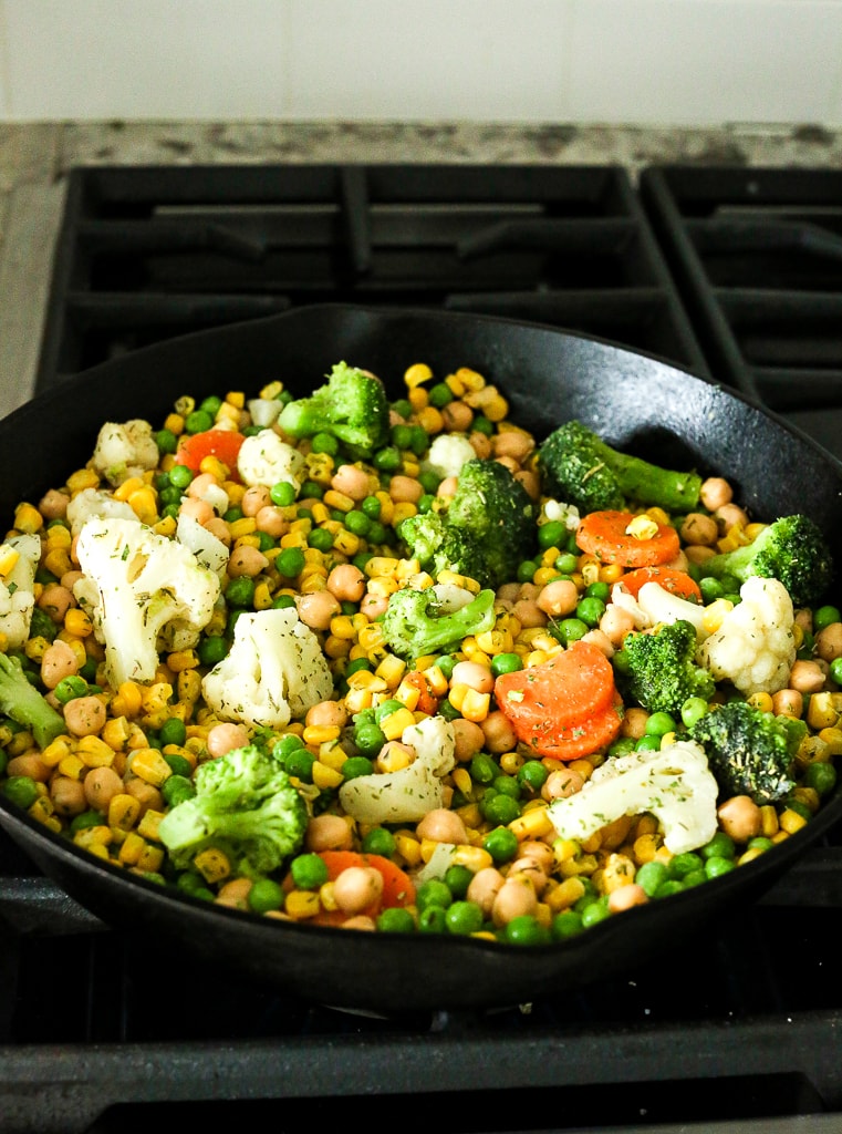 vegetables and chickpeas in a cast iron skillet on a stovetop